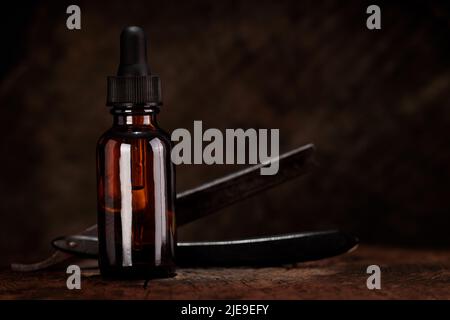 Barbershop concept. Barber tools, razor and bottle of beard oil on dark wooden background. Stock Photo