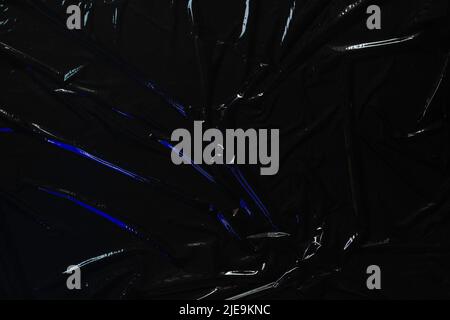Transparent plastic wrap on black background. Crumpled wrinkled plastic cellophane. Reflecting blue color light and shadow on creases and folds in Stock Photo