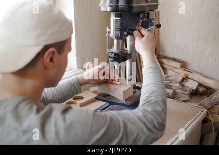 A young carpenter uses a drilling machine to drill holes in a wooden board Stock Photo