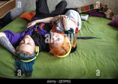 Portrait of a young tattooed punk couple girl and guy with long dyed braided hair lying on a large bed top view. Stylish modern youth Stock Photo