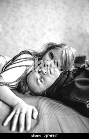 Portrait of a young tattooed punk couple of a girl and a guy with long dyed hair braided, lying on a large bed. Stylish modern youth Stock Photo