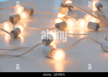 Lighted white bulbs joined by a continuous cable. Several lit light bulbs posing randomly on a reflective white surface. Ideal for representing ideas. Stock Photo