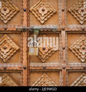 Fragment of minimalist wood carving design on antique timber gate. Vintage wooden entrance door with padlock Stock Photo