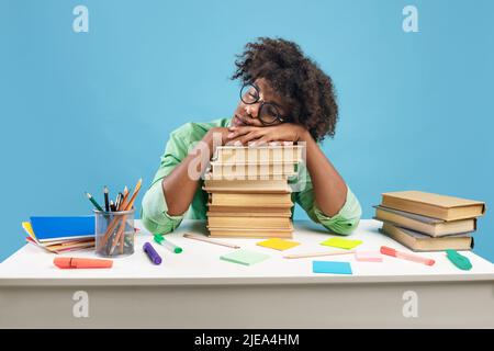 Exhausted black male student sleeping on desk on stacks of books, being tired while preparing for exam Stock Photo