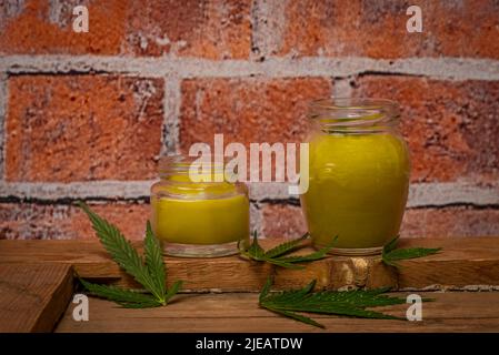 New fresh marijuana salve in glass on old wooden dirty table near brick wall Stock Photo