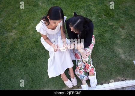Top view of two asian women using a mobile while sitting on the grass of a park Stock Photo