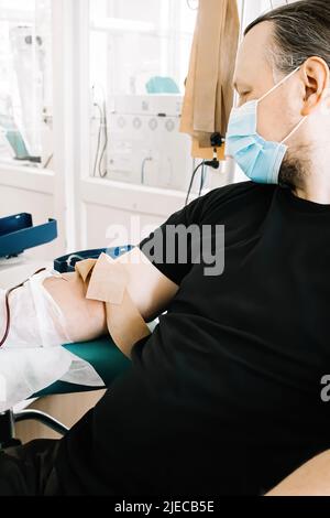 Middle-aged man donates blood in medical laboratory. Blood donor donates blood for life saving and medical research. International Blood Donation Day. Stock Photo