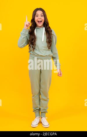 Amazed teen girl. Excited expression, cheerful and glad. Full length of attractive cheerful girl in sport wear isolated over yellow background Stock Photo