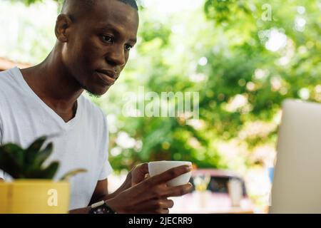 Confident and successful multiracial businessman drinking coffee and work, chatting online using laptop in street cafe Stock Photo