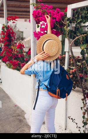 Tourist woman admiring blooming pink bougainvillea flowers on Santorini island, Greece. Backpacker walking in city Stock Photo