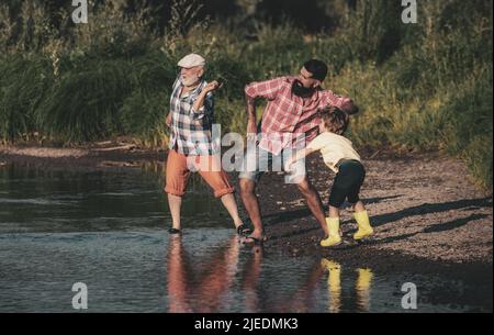 Male Child with Father and Grandfather Skipping Stones on Water. Man in different ages. Stock Photo