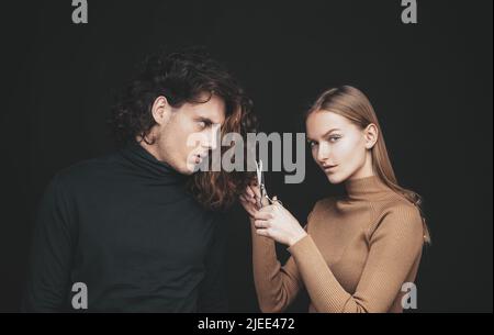 Girl scheming an evil plan of cutting off a curly hair in a man. A smart wily woman has wonderful schemes like a crook of a friend, a dark background Stock Photo