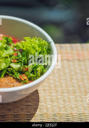 VERTICAL Ceramic white light bowl with mix green lettuce leaves, spinach leaf salad ingredients fresh vegetables pureed red tomato serving plate Stock Photo