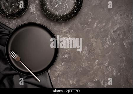 Craft ceramic handmade concept. Empty black ceramic plate on black dining table background. top view Stock Photo