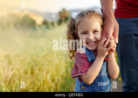 Little girl holding fathers hand,looking camera,smiling.Happy family, bonding, love. Summertime. Dad and daughter. Fathers day. Stock Photo