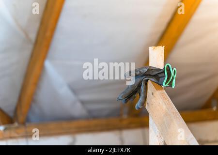 Black torn construction rubberized gloves hang against the background of an uninsulated roof Stock Photo