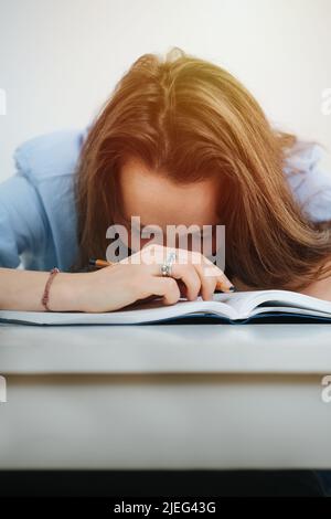 Napping business woman in blue dress shirt fell asleep while writing in a journal. Lying on a desk. Stock Photo