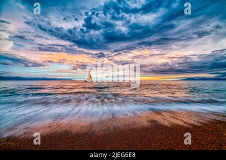 A Sailboat Sails Along The Ocean With A Colorful Cloudscape Overhead Stock Photo