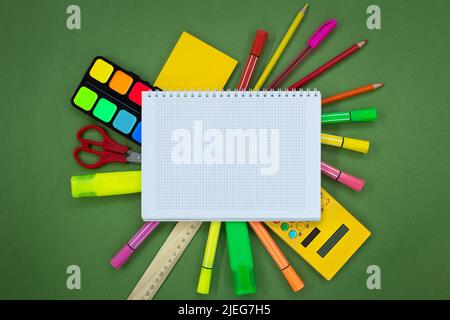 Set of stationery around a notebook on a green background. Pens, markers, felt-tip pens, scissors, calculator, paints. Back to school concept. Copy sp Stock Photo