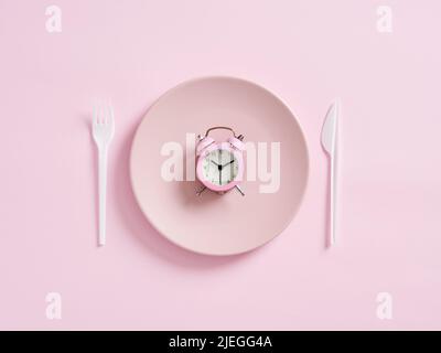 Alarm clock on pink plate with knife and fork. Intermittent fasting, lunchtime, weight loss, meal plan or diet concept. Stock Photo