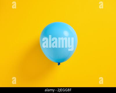 Blue inflated balloon on yellow background. Stock Photo