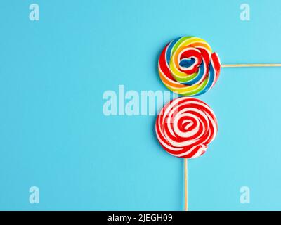 Rainbow and red white colored swirl round candy lollipops on blue background. Stock Photo