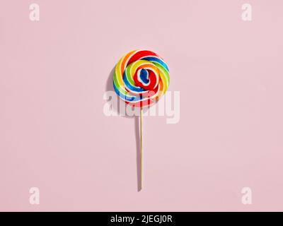 Rainbow colored swirl round candy lollipop on pink background. Stock Photo