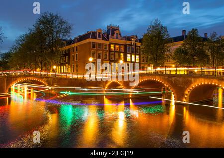 Netherlands. Summer night in Amsterdam. Busy movement of boats under bridges and cars on the embankment. Long exposure headlight and taillight trails Stock Photo