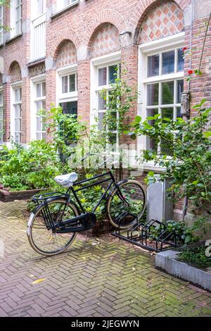 Bicycle parked in a bike stand front of a building, Amsterdam city neighborhood. Traditional red brick wall house, paved alley. Holland Netherlands Stock Photo