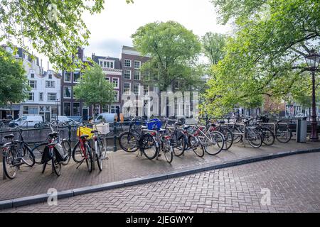Bicycles parked on a canal bridge. Amsterdam traditional brick facade houses background. Sunny day, Netherlands Holland Stock Photo