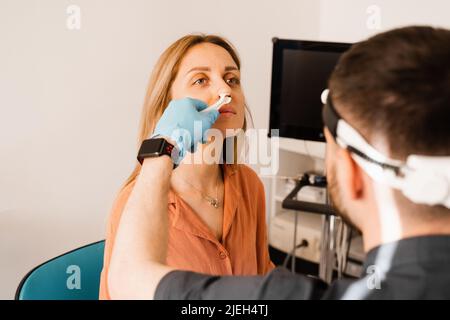 Rhinoscopy of woman nose. Consultation with doctor. Otolaryngologist examines girl nose before procedure of endoscopy of nose Stock Photo