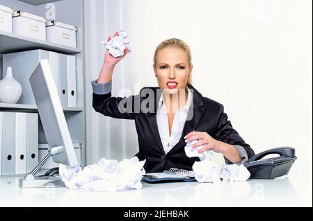 Eine Frau im Büro wirft mit Papierknäuel. Ärger, Stress und Frust am Arbeitsplatz