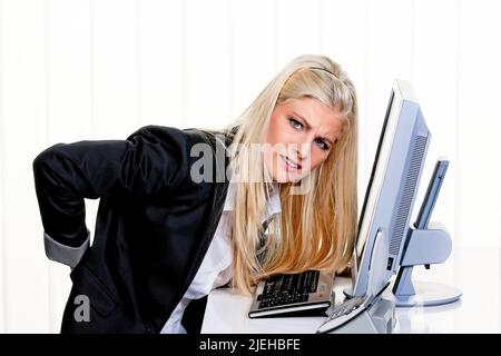 Eine junge Frau sitzt im Büro und hat Rückenschmerzen Stock Photo