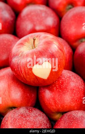 Ein roter Apfel mit Herz liegt auf anderen roten Äpfeln, Obst, Frucht, Früchte, Liebesapfel, Stock Photo
