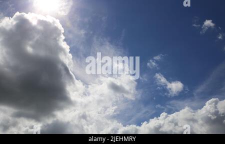 Dramatic blue clear summer sky after rain background, sun breaking through white fluffy cumulus morning clouds Stock Photo