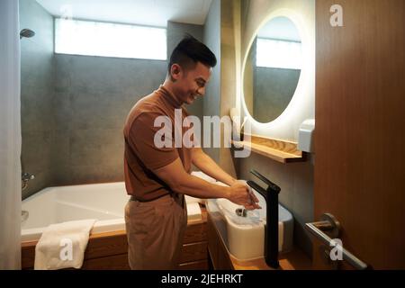 Positive young man washing hands after coming home from work Stock Photo