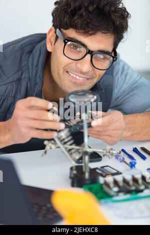 male technician examining circuit board looking through magnifying glass Stock Photo