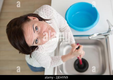woman using plunger in blocked kitchen sink Stock Photo