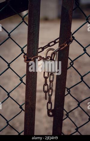 Close-up of a locked rusty old gate tethered by a chain and padlock with blurred background. Image in brown tones with vertical orientation Stock Photo