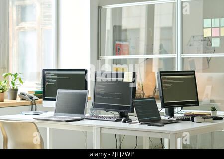 Horizontal image of workplace of IT specialist with codes on screens of computers and laptops on table Stock Photo