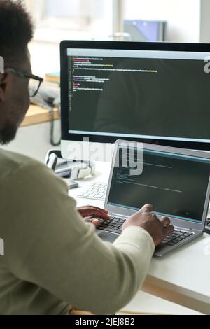 Rear view of young programmer sitting at table and typing on laptop, he working with codes to develop new software Stock Photo