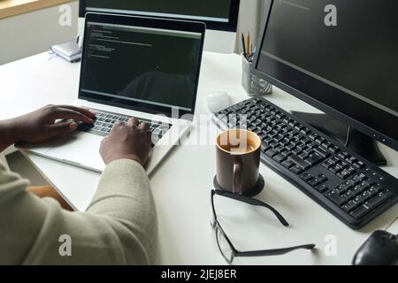 Close-up of programmer sitting at his workplace with cup of coffee and writing codes on laptop Stock Photo