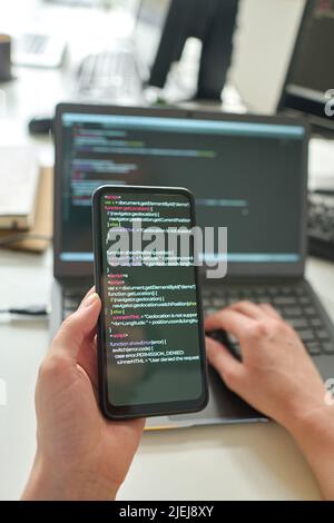 Close-up of programmer using computer codes on his smartphone to install software program on laptop Stock Photo