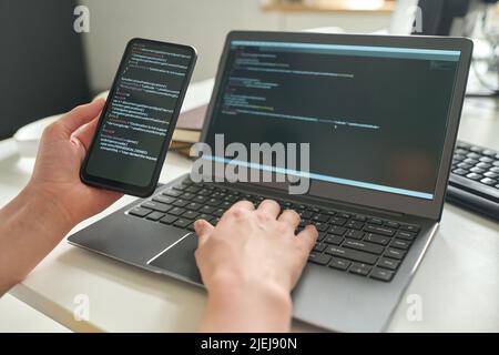Close-up of developer connecting her smartphone with computer codes to laptop at her workplace Stock Photo