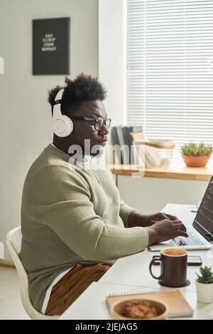 African young software developer in wireless headphones concentrating on his online work on laptop Stock Photo