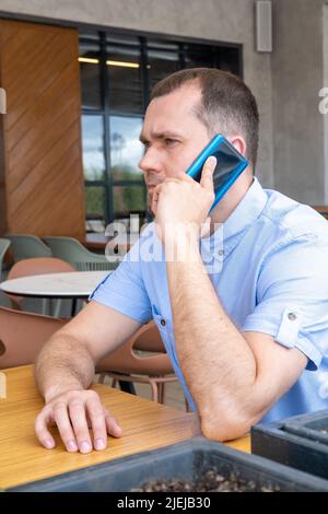 A middle-aged Arab man with a beard is talking on the phone in an outdoor cafe. Smiling middle aged businessman freelancer using mobile phone Stock Photo