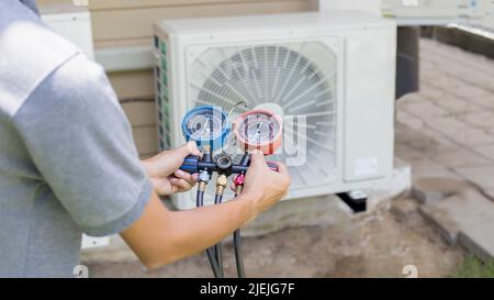 Air repair mechanic using measuring equipment for filling industrial factory air conditioners and checking maintenance outdoor air compressor unit. Stock Photo