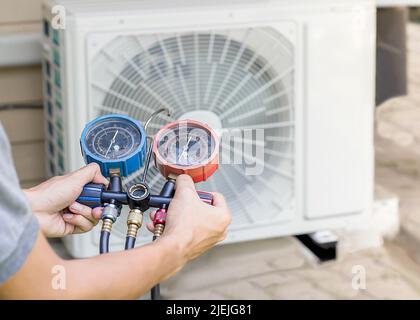 Air repair mechanic using measuring equipment for filling industrial factory air conditioners and checking maintenance outdoor air compressor unit. Stock Photo