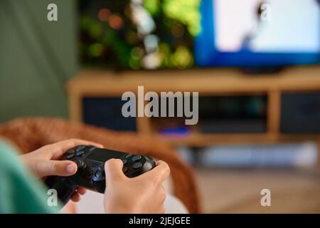 Boy playing video game on console with joyctick gamepad in his hand, Online entertainment and leisure activity, Gambling addiction Stock Photo