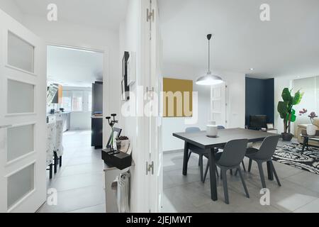 Distributor of a modern house with a living room with a wooden dining table with resin chairs and access to a kitchen with an office Stock Photo
